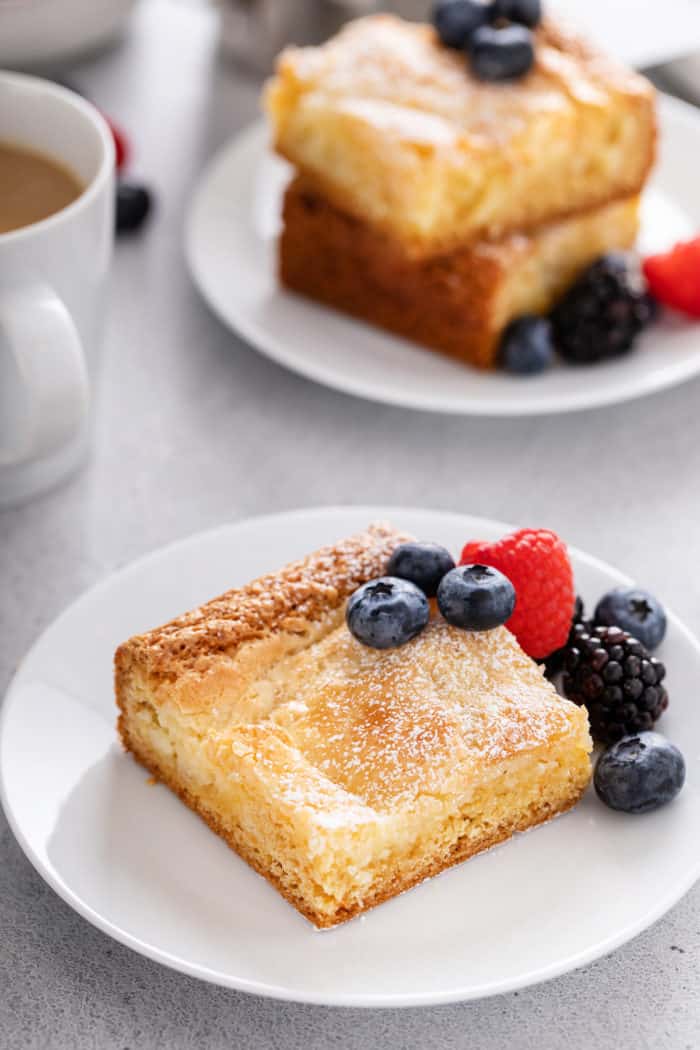 Slice of gooey butter cake on a white plate, garnished with fresh berries.