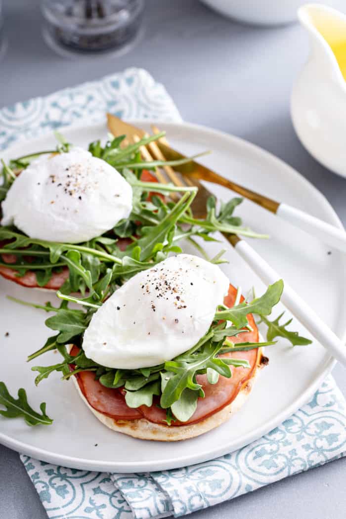 Two poached eggs on top of arugula and canadian bacon on english muffins.