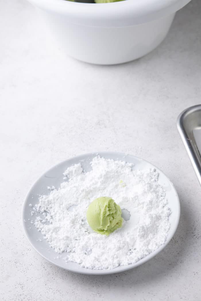 Ball of crinkle cookie dough being rolled in a bowl of powdered sugar.