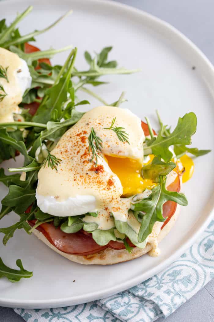 Plated eggs benedict with the egg cut so the yolk is running out over the arugula, candian bacon, and english muffin.