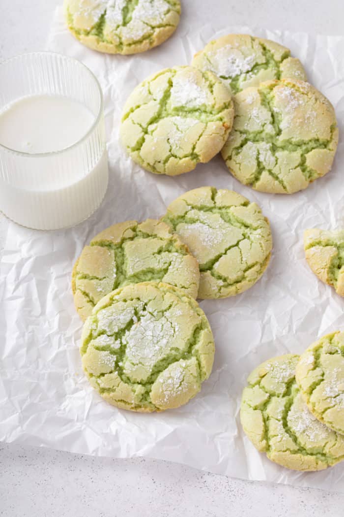 Several green crinkle cookies next to a glass of milk on a piece of parchment paper.