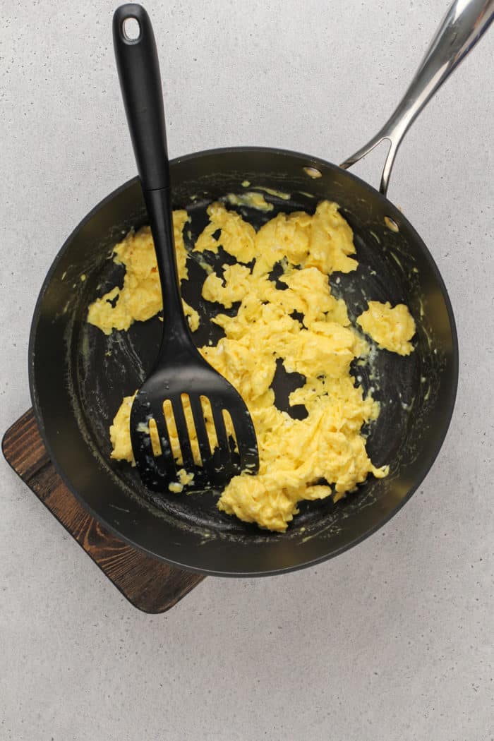 Scrambled eggs being stirred in a black skillet.