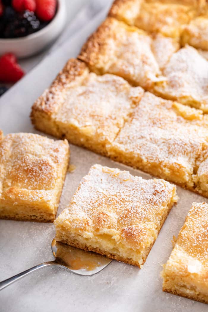 Sliced gooey butter cake, with a cake server about to lift up a slice of the cake.