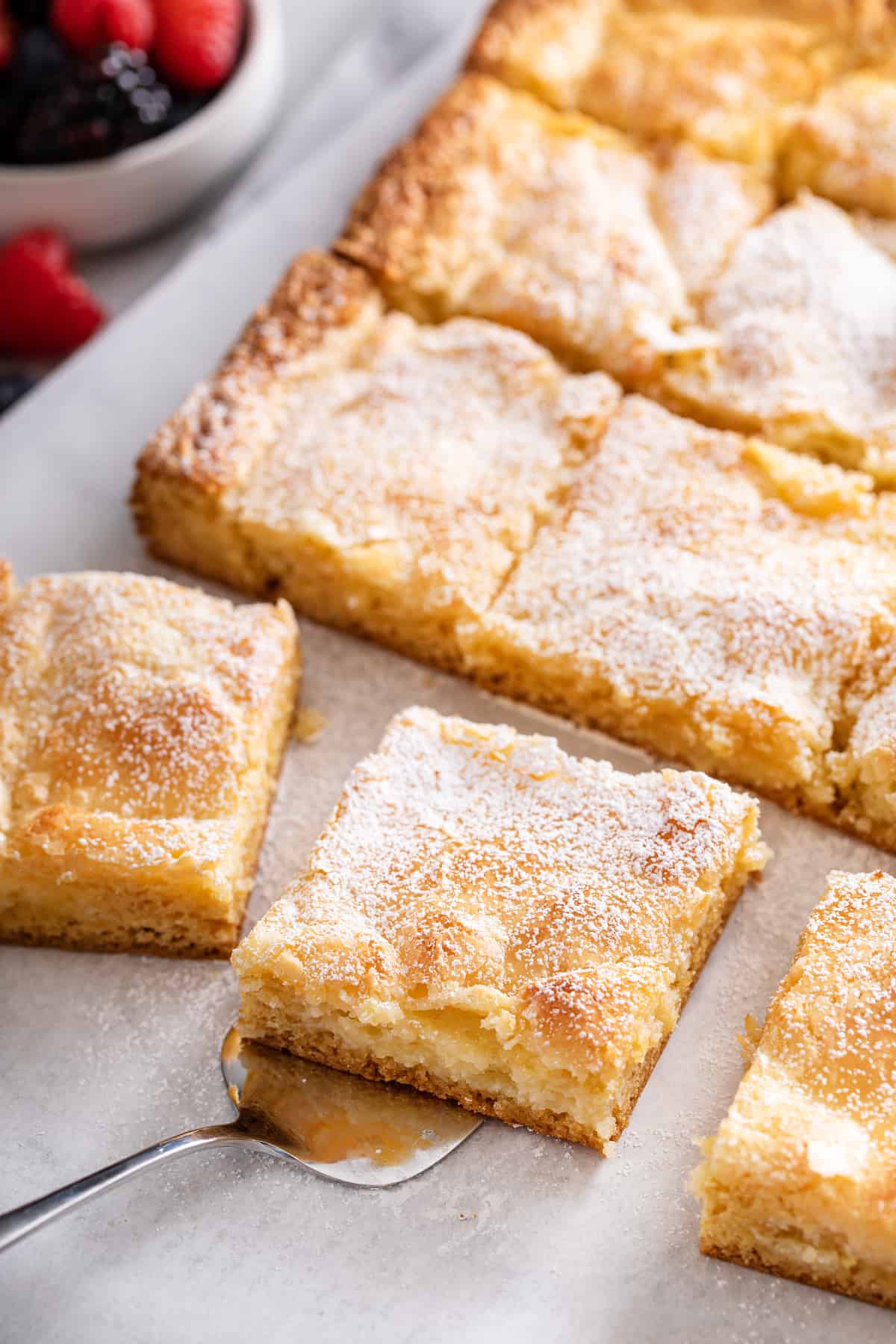 Sliced gooey butter cake, with a cake server about to lift up a slice of the cake.