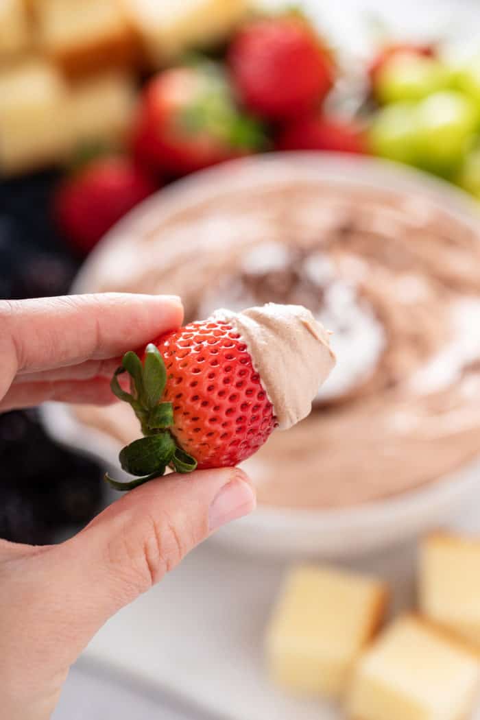 Strawberry dipped in nutella fruit dip being held up to the camera.