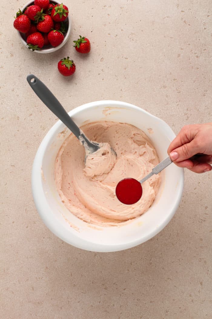 Strawberry puree being added to a white mixing bowl filled with strawberry frosting.