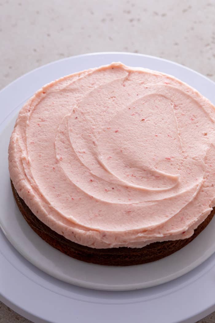 Strawberry frosting spread onto one layer of strawberry cake.