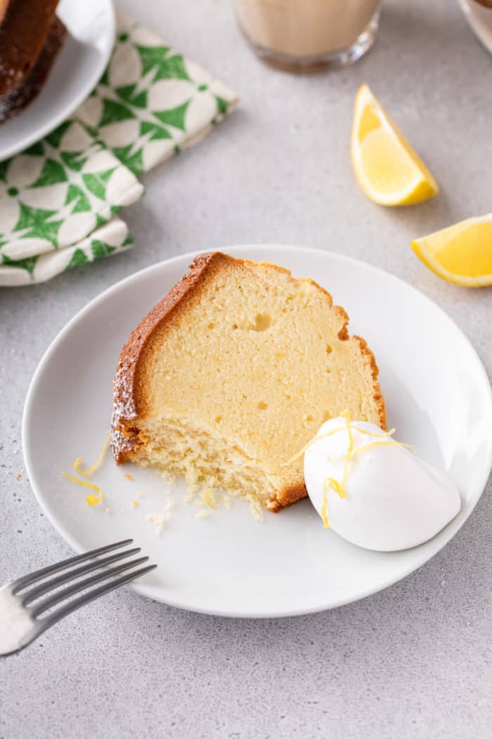 Slice of lemon cream cheese pound cake with a bite taken from it next to a dollop of whipped cream on a white plate.