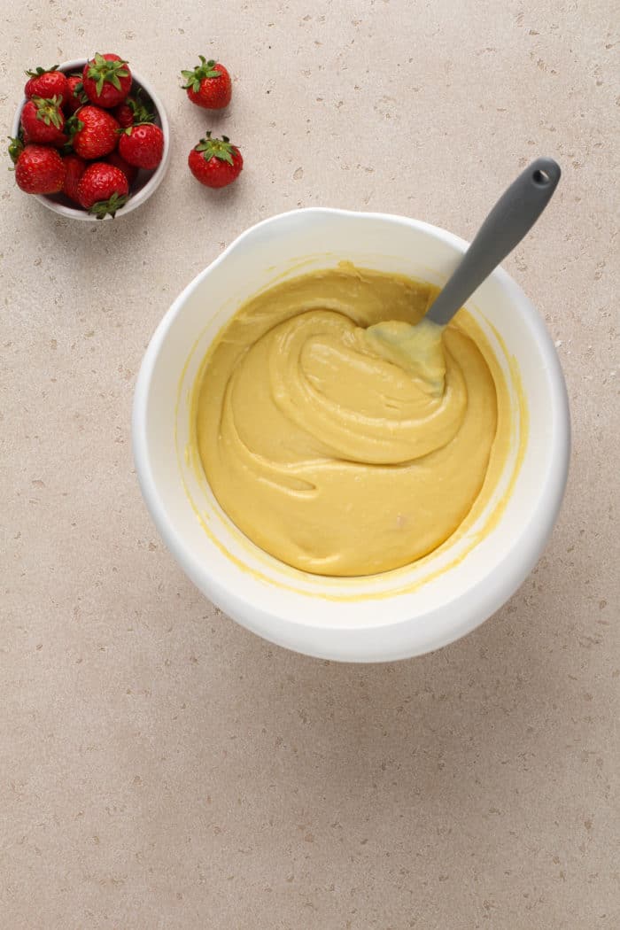 Cake batter in a white bowl set next to a bowl of strawberries.