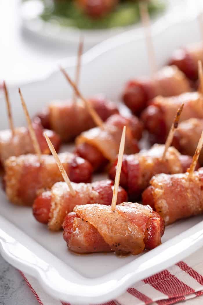 Close up of bacon-wrapped little smokies arranged on a white platter.