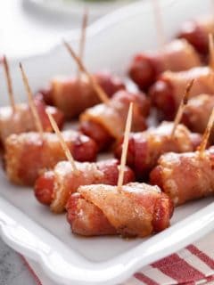 Close up of bacon-wrapped little smokies arranged on a white platter.