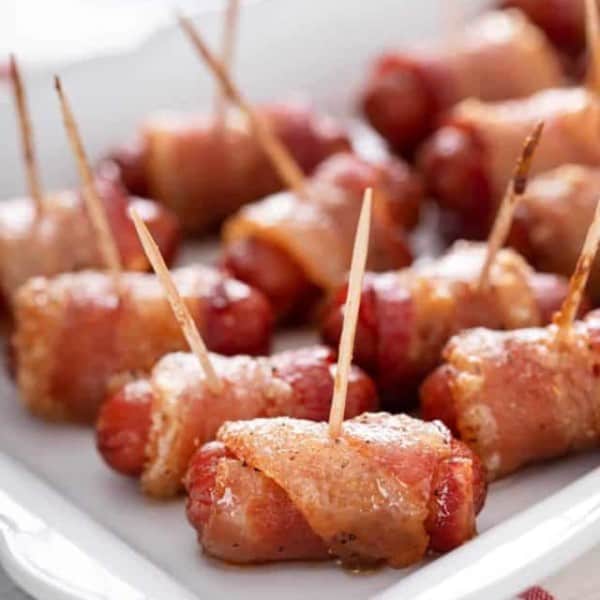 Close up of bacon-wrapped little smokies arranged on a white platter.