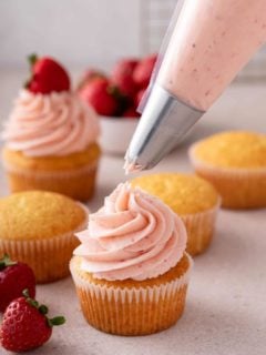 Strawberry frosting being piped onto a vanilla cupcake.