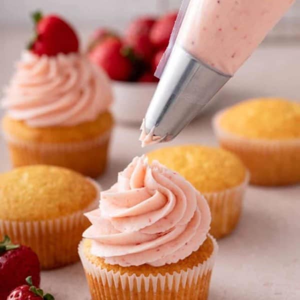 Strawberry frosting being piped onto a vanilla cupcake.