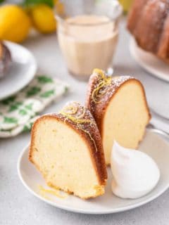 Two slices of lemon cream cheese pound cake garnished with lemon zest and a dollop of whipped cream on a white plate.