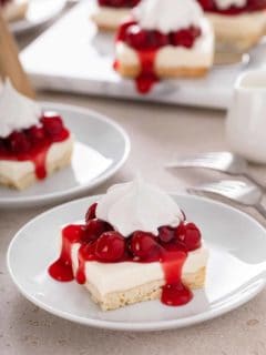 Slices of nana's easy cheesecake topped with cherry pie filling and whipped topping on white plates.