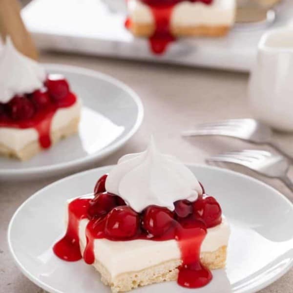 Slices of nana's easy cheesecake topped with cherry pie filling and whipped topping on white plates.