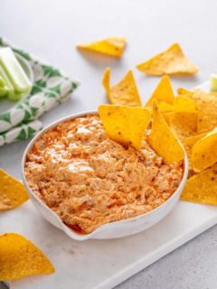 White bowl of slow cooker buffalo chicken dip with two tortilla chips in it.