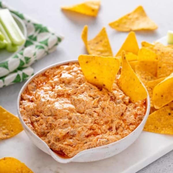 White bowl of slow cooker buffalo chicken dip with two tortilla chips in it.