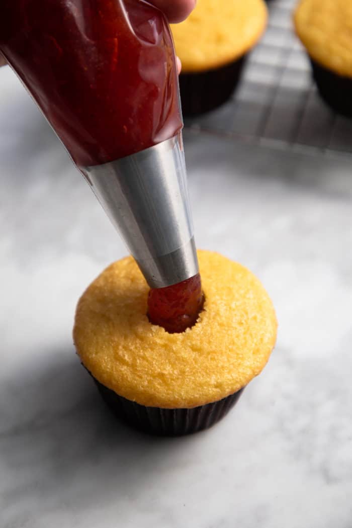 Jam being piped into a hollowed-out cupcake.