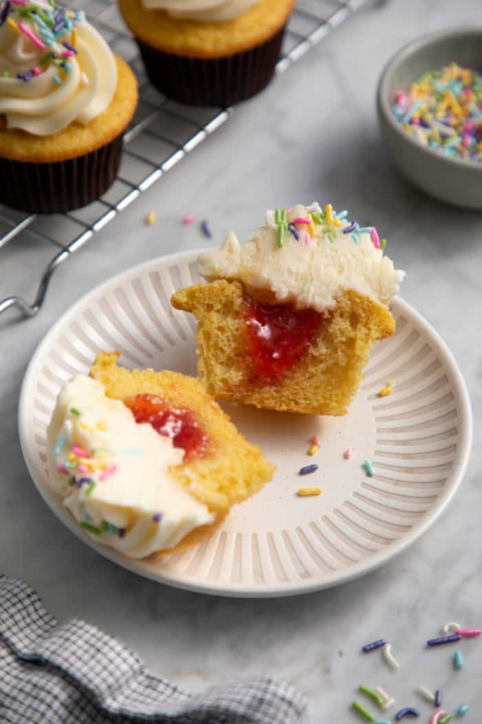 Cupcake filled with strawberry jam cut in half and set on a white plate.