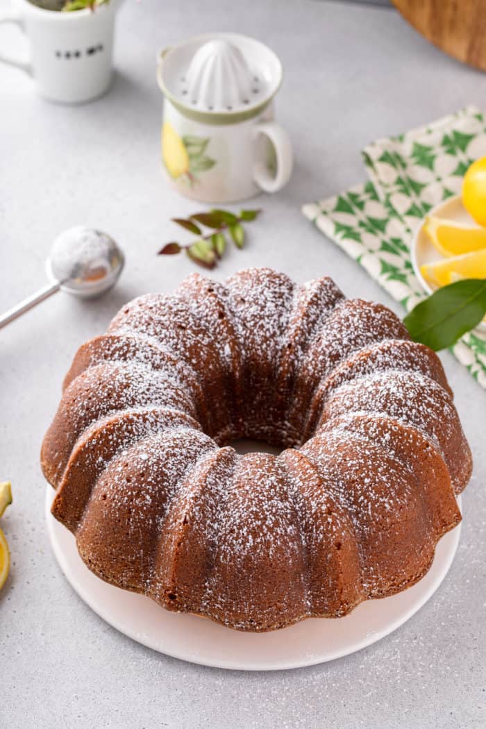 Baked lemon cream cheese pound cake dusted with powdered sugar on a white cake plate.