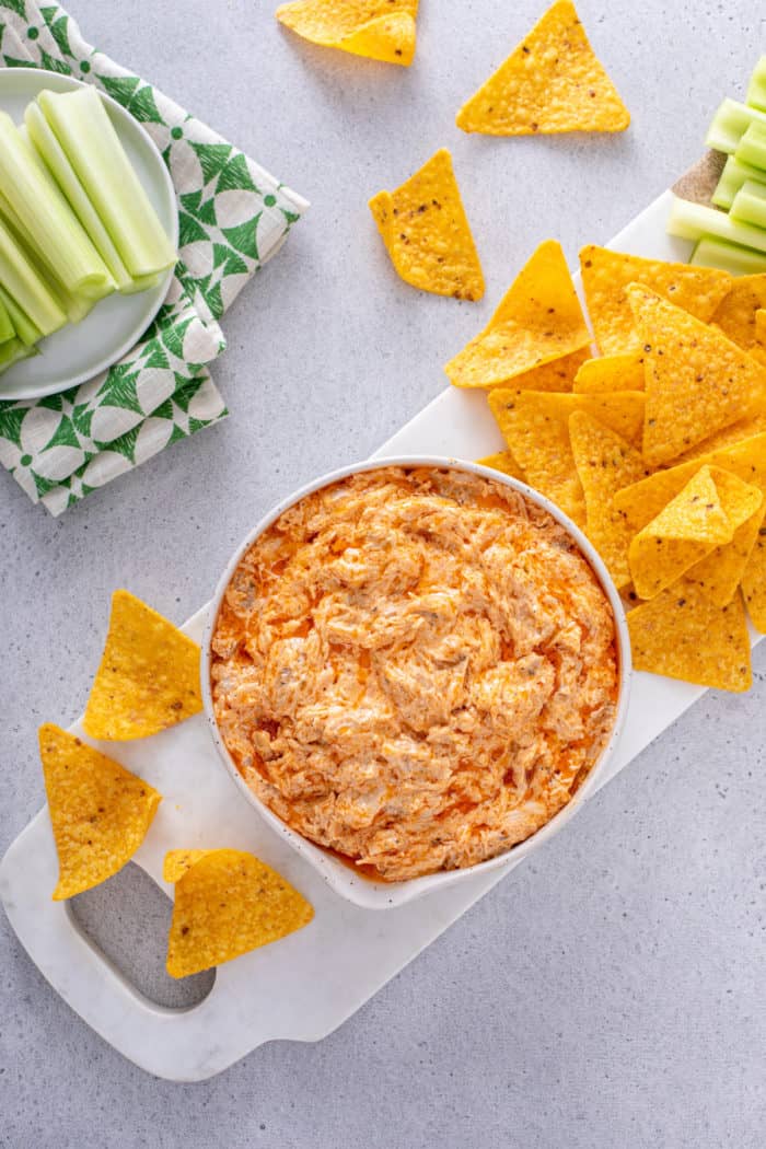 Overhead view of a bowl of buffalo chicken dip on a white cutting board, surrounded by tortilla chips.