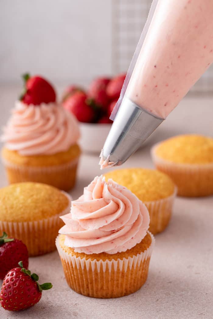 Strawberry frosting being piped onto a vanilla cupcake.