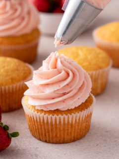 Strawberry frosting being piped onto a cupcake.