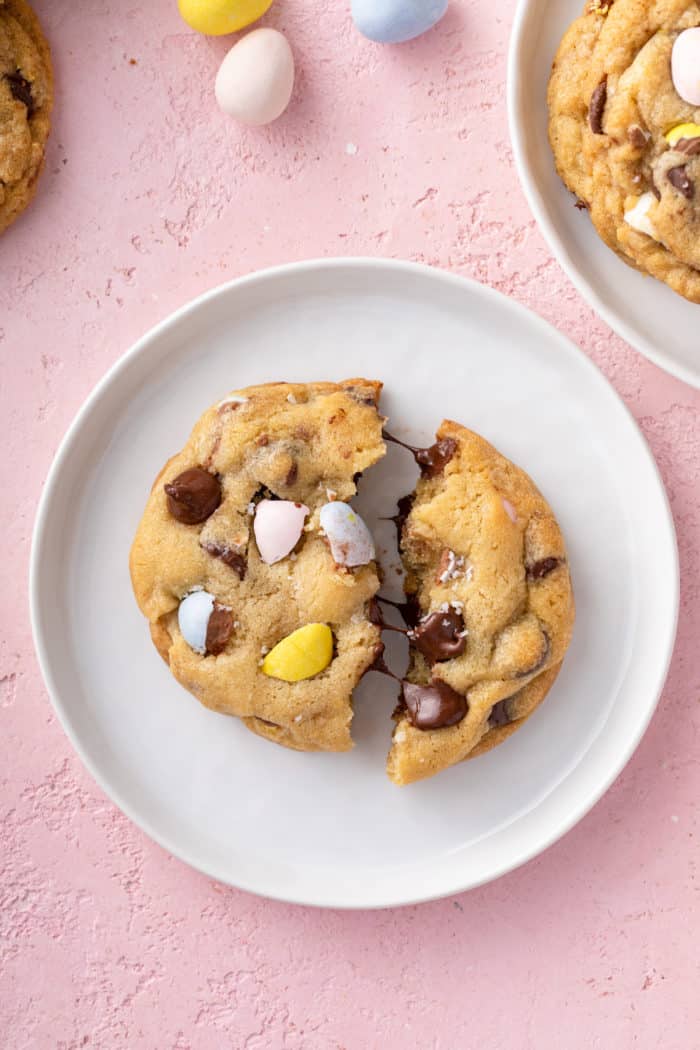 Cadbury egg cookie broken in half on a white plate, showing the melty chocolate chips in the center.