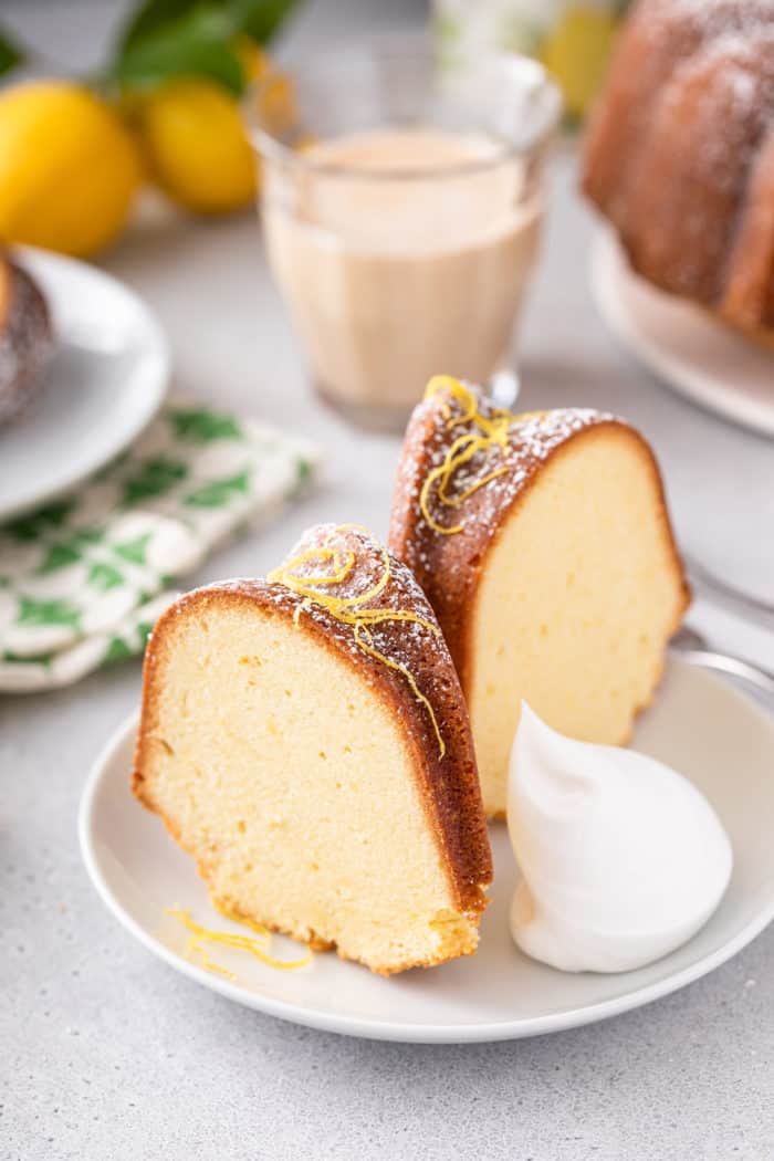 Two slices of lemon cream cheese pound cake garnished with lemon zest and a dollop of whipped cream on a white plate.