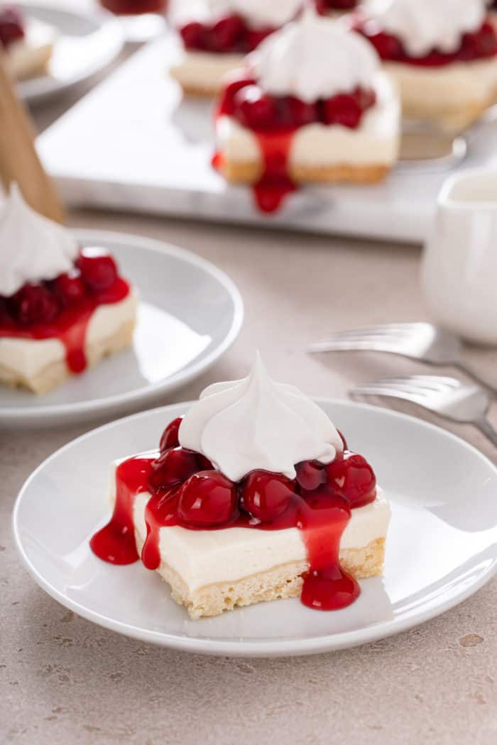 Slices of nana's easy cheesecake topped with cherry pie filling and whipped topping on white plates.