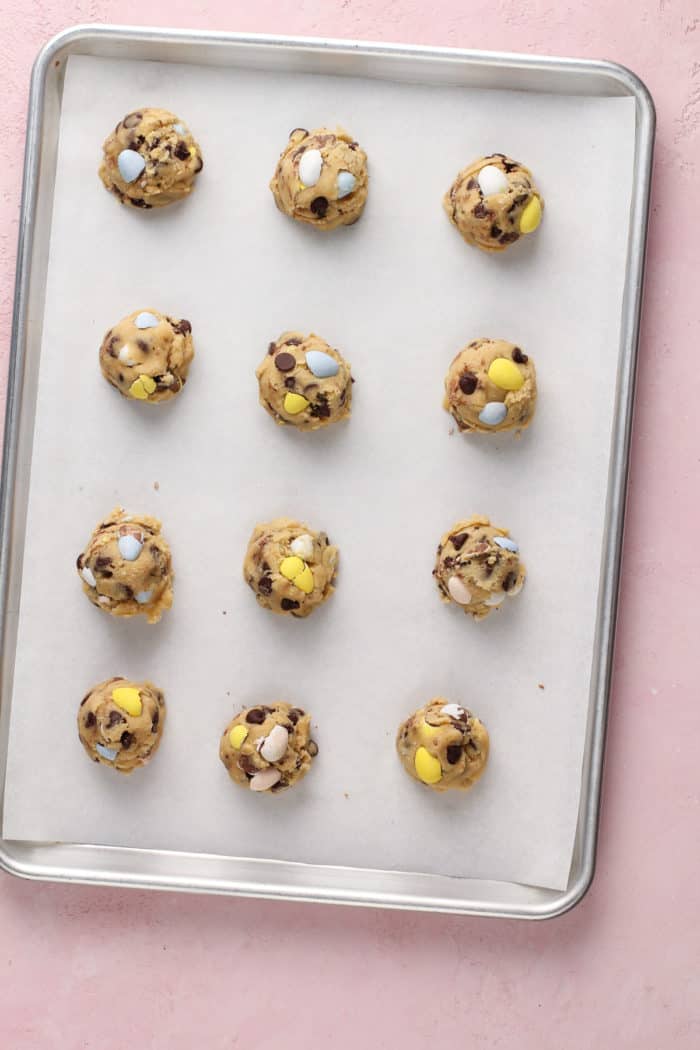 Balls of cadbury egg cookie dough portioned onto a parchment-lined baking sheet.