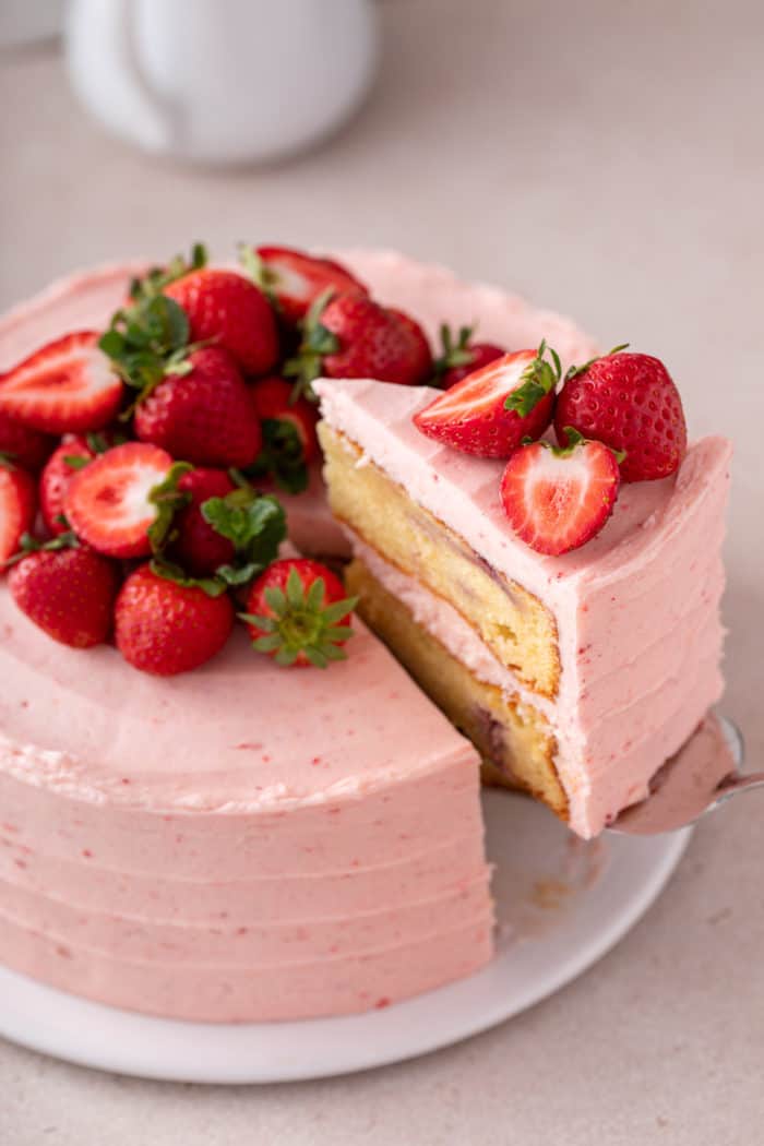 Cake server lifting up a slice of cake from a strawberry layer cake.