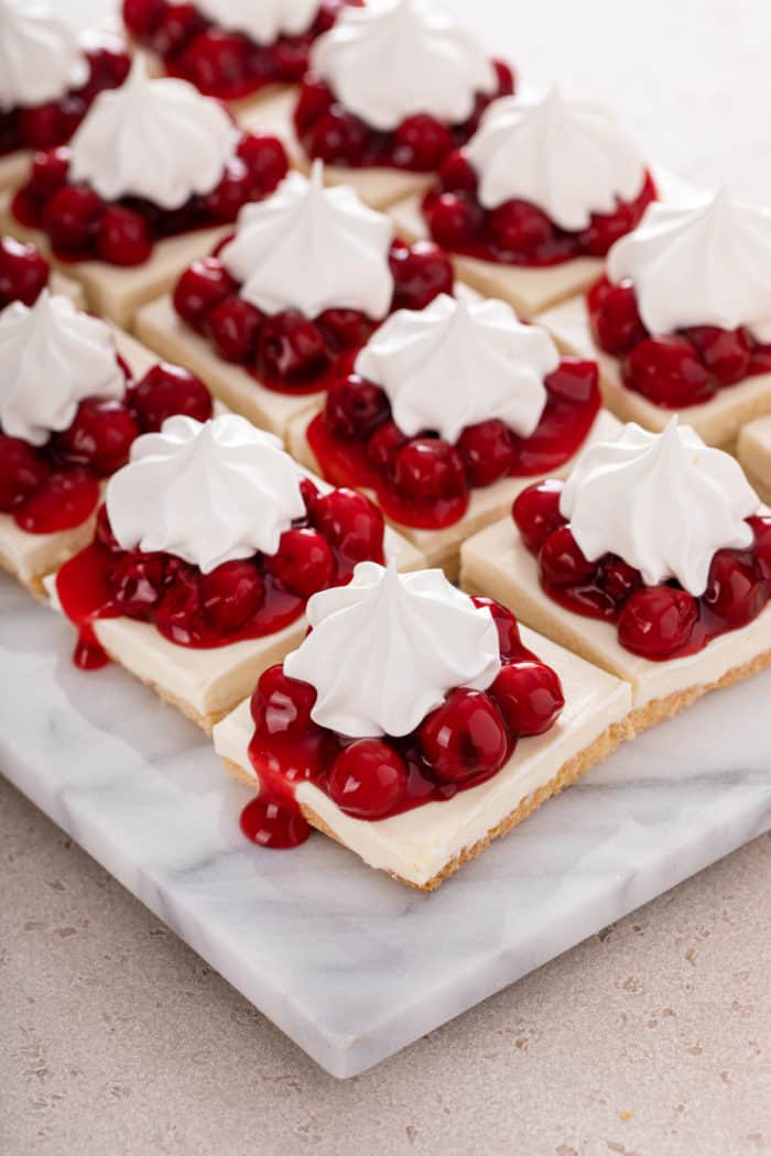 Slices of nana's easy cheesecake topped with cherry pie filling and whipped topping set on a marble platter.
