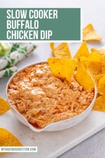 White bowl of slow cooker buffalo chicken dip with two tortilla chips in it. Text overlay includes recipe name.