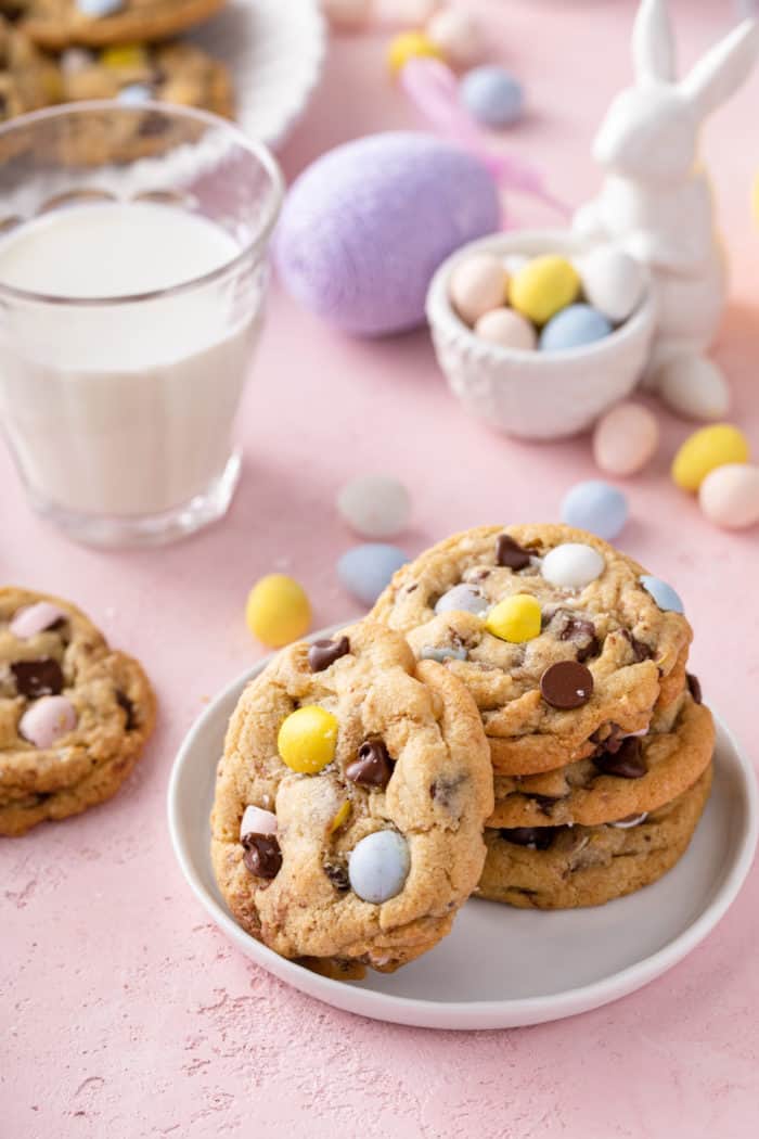 White plate with a stack of cadbury egg cookies on it set on a countertop in front of a glass of milk and a small bowl of cadbury mini eggs.