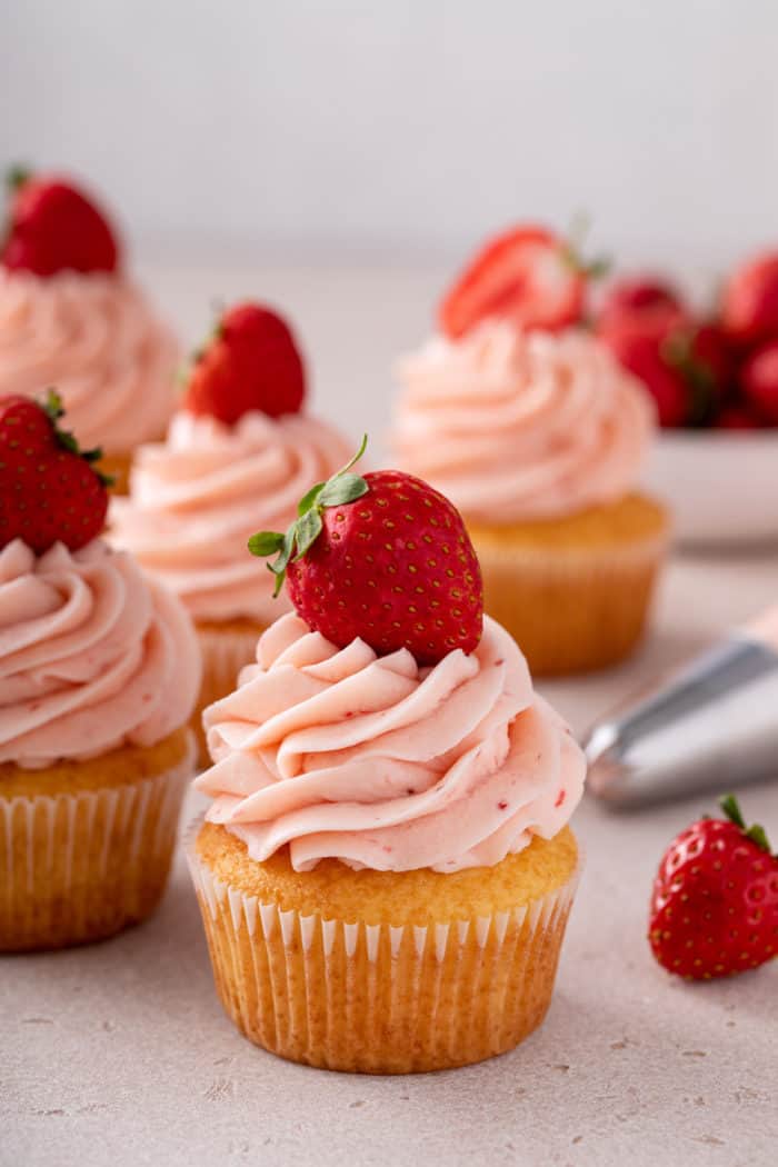 Vanilla cupcakes topped with strawberry frosting and garnished with fresh strawberries.