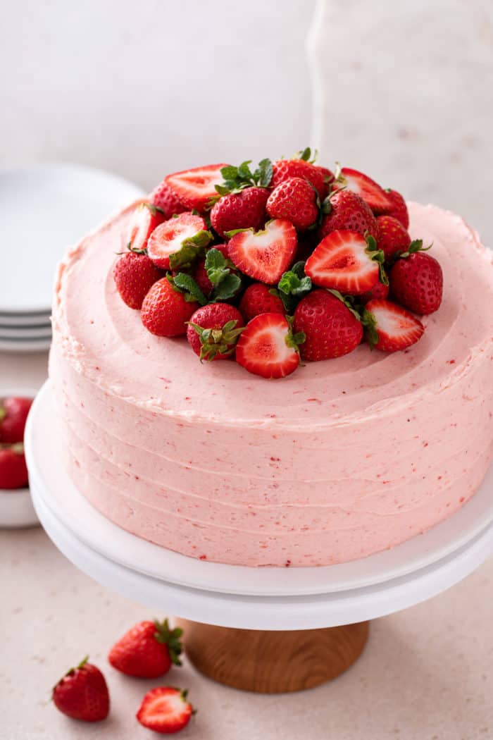 Strawberry layer cake decorated with fresh strawberries on a white cake plate.