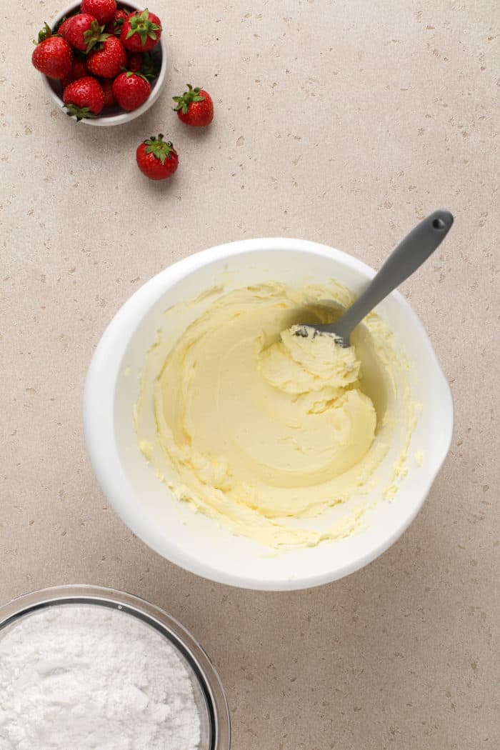 Beaten butter in a white mixing bowl for strawberry frosting.