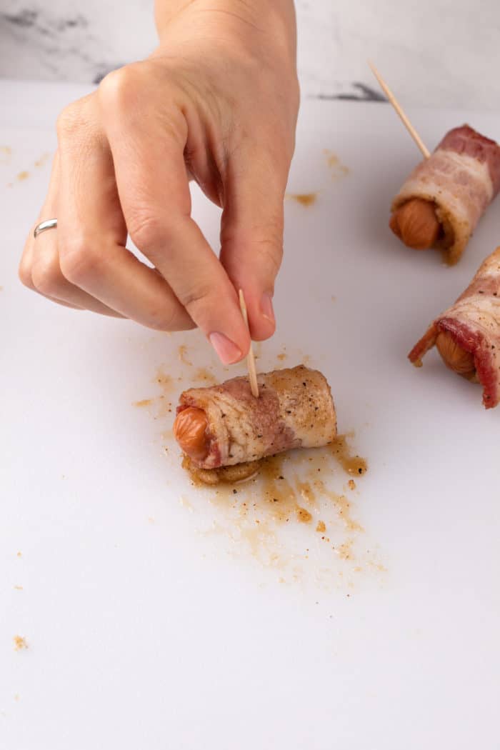 Toothpick being inserted into a little smokie sausage that was just wrapped in bacon.