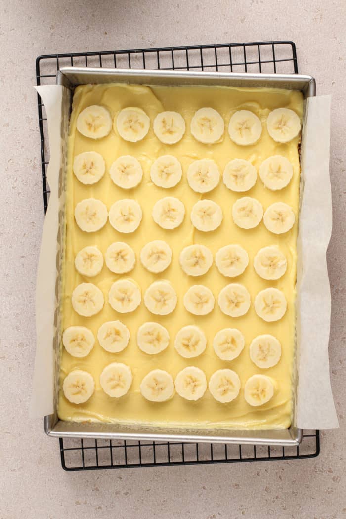 Sliced bananas layered on top of vanilla pudding filling in a pan.