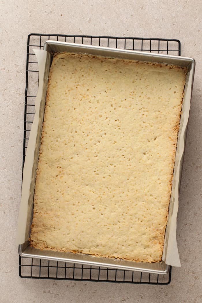 Baked shortbread crust in a metal pan, set on a cooling rack.