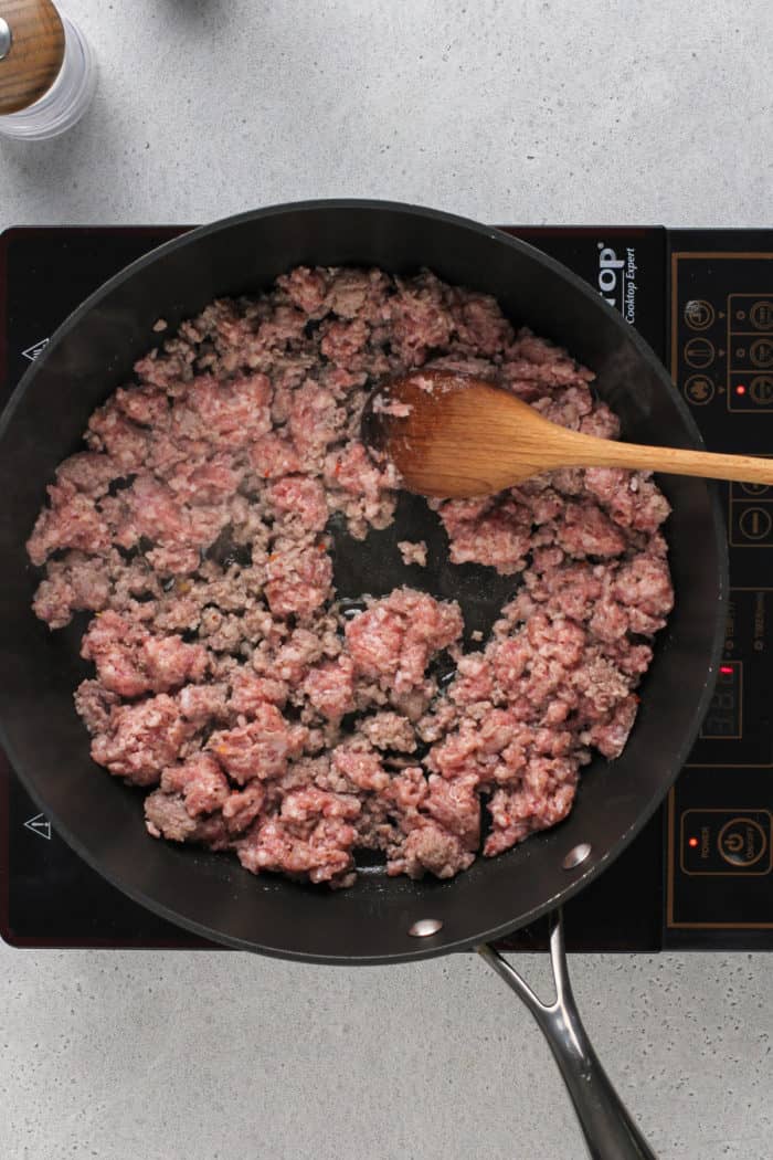 Sausage being cooked in a black skillet on an induction burner.