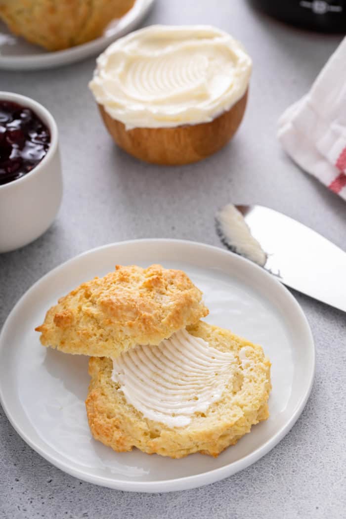 Buttermilk drop biscuit cut in half and spread with butter on a white plate.