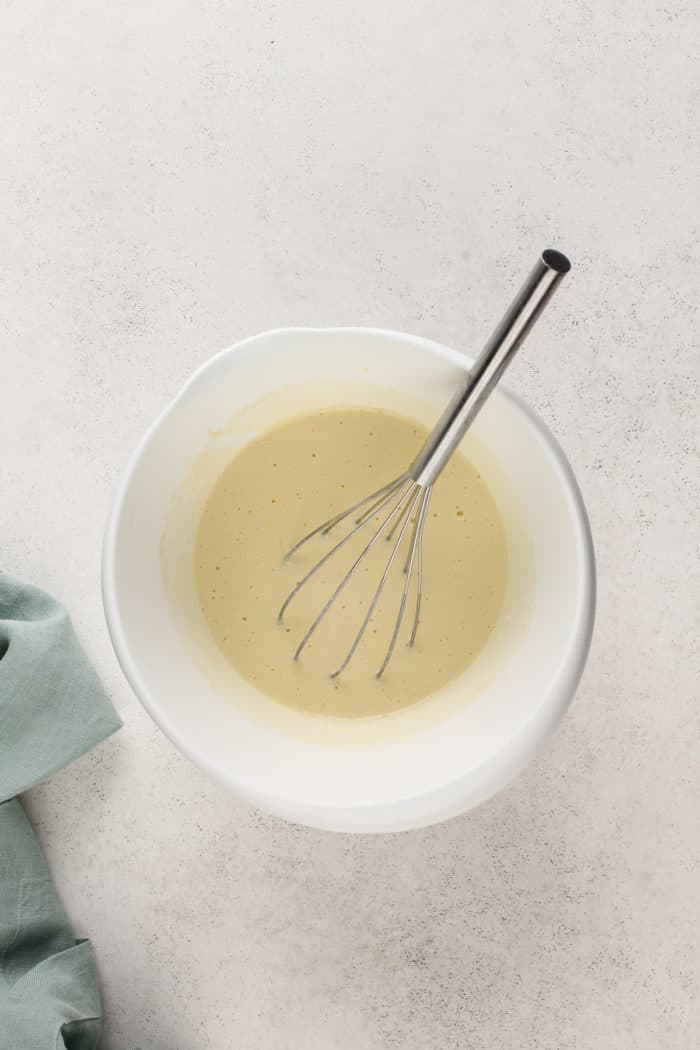 Wet ingredients for buttermilk pancakes being whisked in a white mixing bowl.