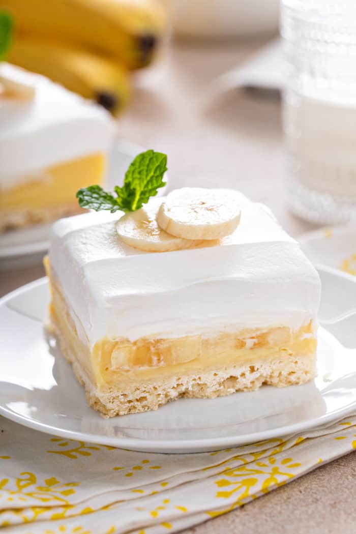 Banana cream bar set on a white plate so you can see the layers of crust, filling, and topping.