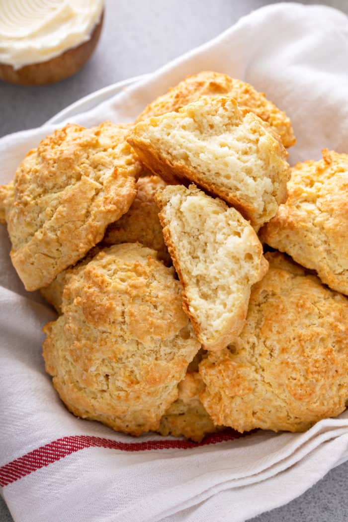 Basket of buttermilk drop biscuits with one of the biscuits broken in half to show the crumb texture.