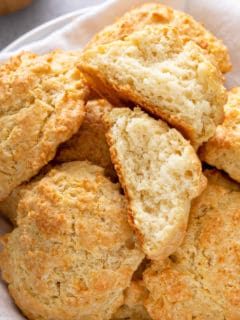 Close up of buttermilk drop biscuits in a basket. One of the biscuits is broken in half to show the light and fluffy texture.