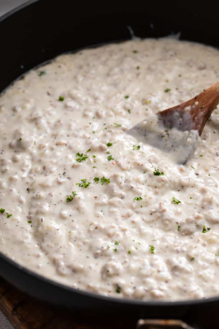 Close up of sausage gravy being stirred with a wooden spoon in a black skillet.